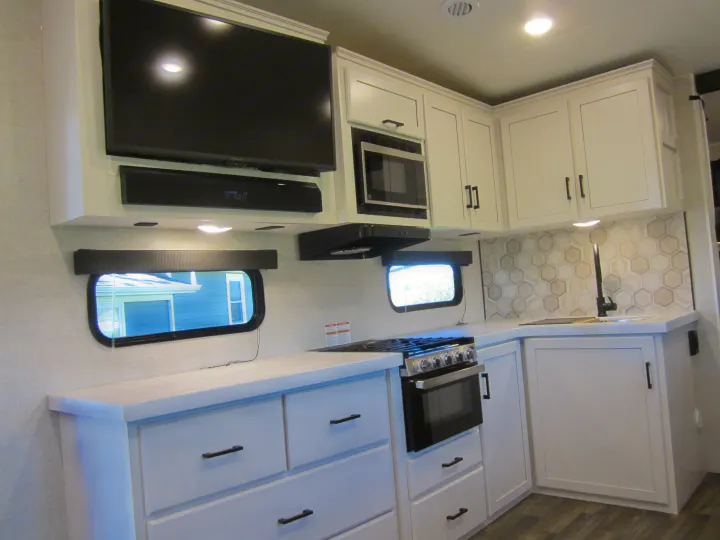 Sleek RV rental kitchen interior: white cabinets, black appliances, hexagon backsplash, and ample counter space.. Jayco Eagle HT 2024