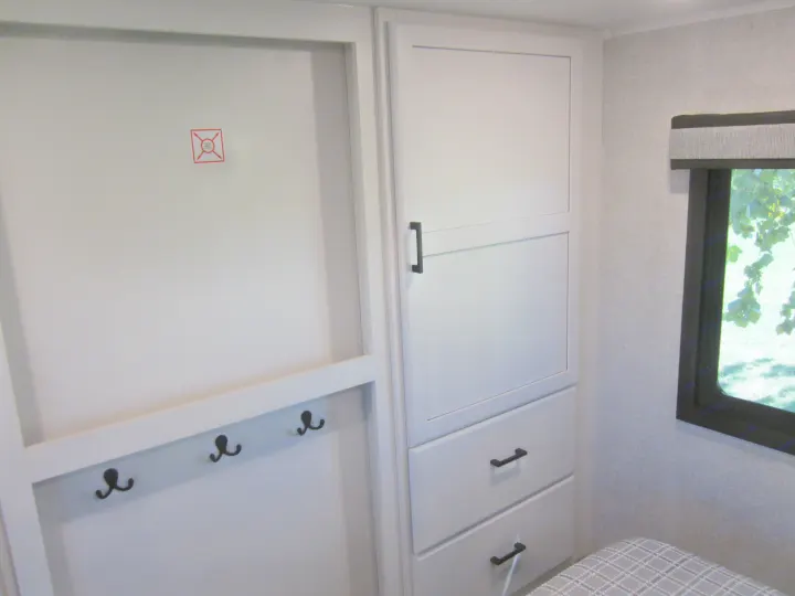 RV rental bedroom showing white storage cabinet, drawers, hooks, safety sign, & window with view.. Jayco Eagle HT 2024