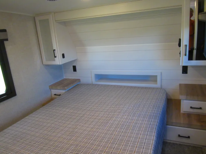 Cozy RV rental bedroom features a plaid bedspread, modern shiplap headboard, and built-in storage.. Jayco Eagle HT 2024