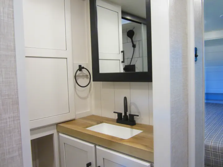 Modern RV rental bathroom with wood-look counter, white sink, and black fixtures. Reflected shower. Clean interior.. Jayco Eagle HT 2024