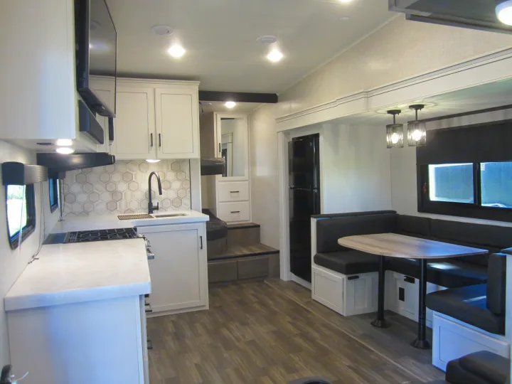 Modern RV rental interior: well-lit kitchen with hexagonal backsplash, U-shaped dining booth, and wood-look floor.. Jayco Eagle HT 2024