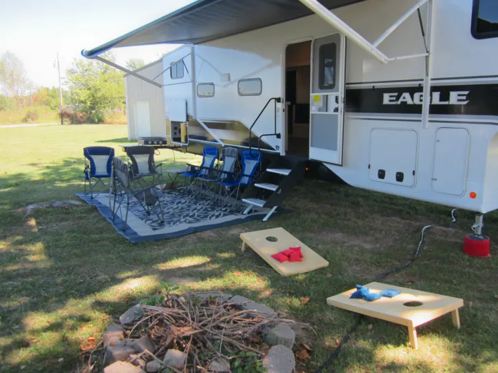 Relaxing **RV rental** site: white camper, extended awning, chairs, cornhole, and a fire pit ready for outdoor enjoyment.. Jayco Eagle HT 2024