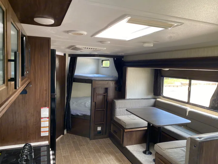 RV rental interior with a cozy dinette, multi-level bunk beds, and a functional kitchen visible on the left.. Forest River Cherokee Grey Wolf 2021