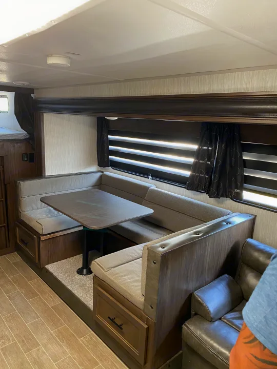 RV rental interior: U-shaped dinette, table, window blinds, bunk bed, and a partial view of a comfy couch.. Forest River Cherokee Grey Wolf 2021