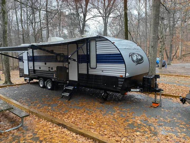Experience nature with this RV rental travel trailer set up in a rainy, leaf-covered forest campsite, perfect for camping.. Forest River Cherokee Grey Wolf 2021