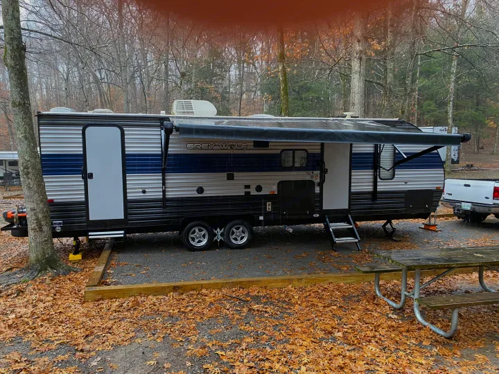 This Grey Wolf RV rental is parked at a fall campsite with wet leaves on the ground and a picnic table.. Forest River Cherokee Grey Wolf 2021
