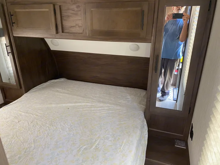 RV rental bedroom interior with a comfortable bed, overhead wood cabinets, and a mirrored wardrobe reflecting the photographer.. Forest River Cherokee Grey Wolf 2021