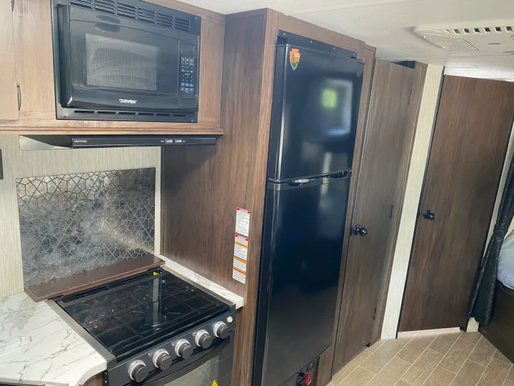 RV rental interior: A fully equipped kitchen with a black microwave, stove, and refrigerator, amidst wood cabinetry.. Forest River Cherokee Grey Wolf 2021