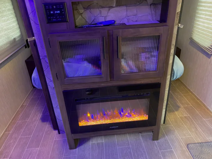 This rv rental features a cozy entertainment unit with an electric fireplace, stone wall, and sleeping areas on each side.. Forest River Cherokee Grey Wolf 2021