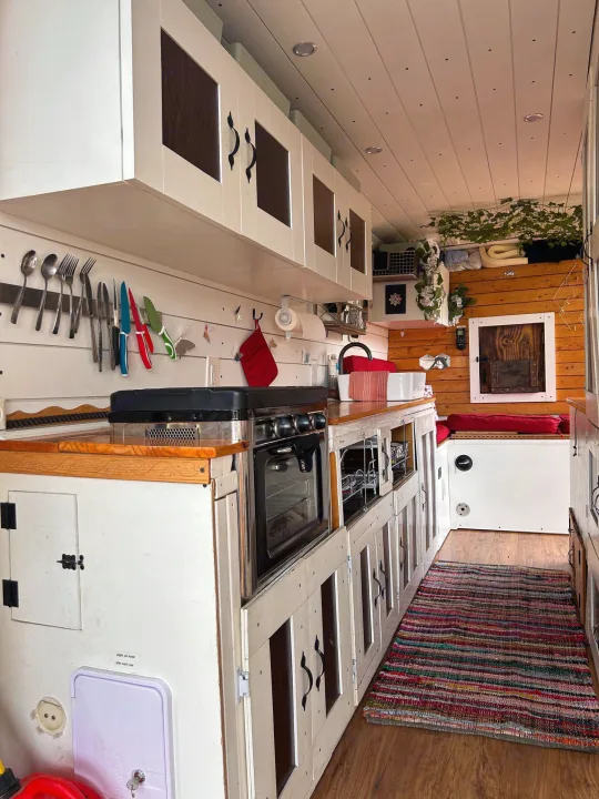 Compact RV rental kitchen with white cabinetry, wooden counters, and a stove/oven, leading to a cozy seating area.. Ram Dodge Promaster 3500 2019