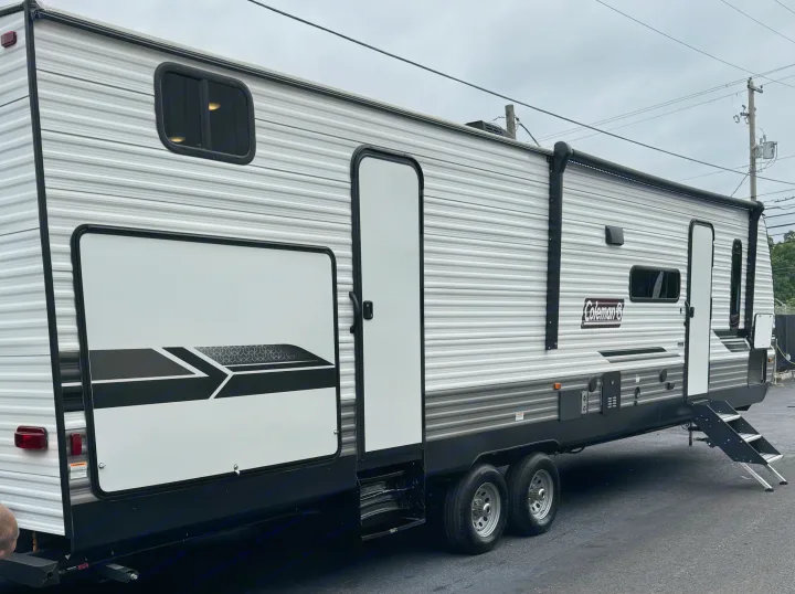 Spacious grey and white travel trailer RV rental, parked outdoors on asphalt, showing its side, awning, and steps.. Coleman Lantern 334BH 2024