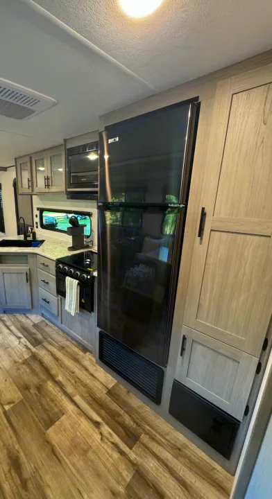 RV rental kitchen: spacious layout with modern black appliances (fridge, oven, microwave), light wood cabinets, and plank flooring.. Coleman Lantern 334BH 2024