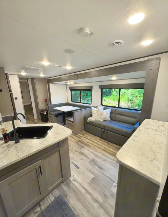 Bright, spacious rv rental interior: modern kitchen, grey and white counters, comfortable dinette, and sofa. Ideal for travel.. Coleman Lantern 334BH 2024