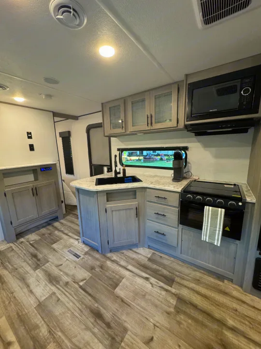 This modern RV rental features a functional, bright kitchen with light cabinets, stove, sink, and microwave oven.. Coleman Lantern 334BH 2024