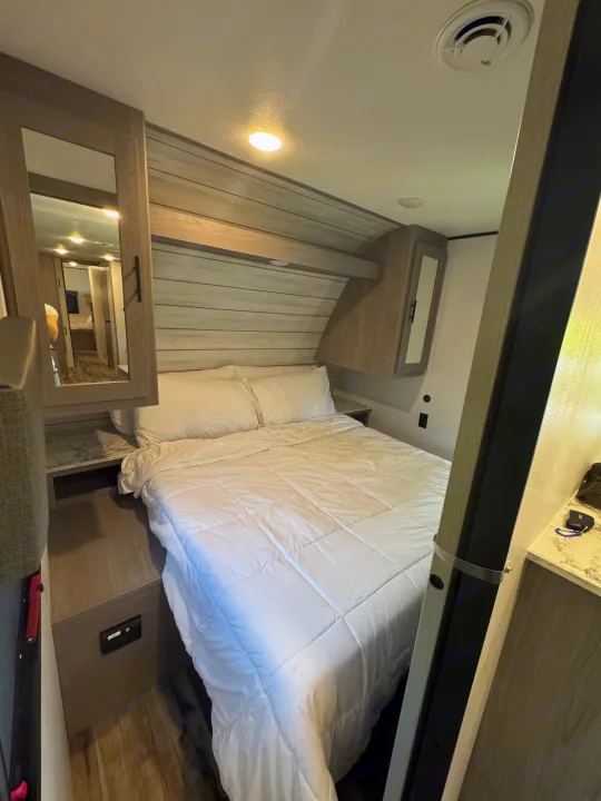 Cozy RV rental bedroom featuring a bed with white bedding, overhead cabinets, and a modern light wood interior.. Coleman Lantern 334BH 2024