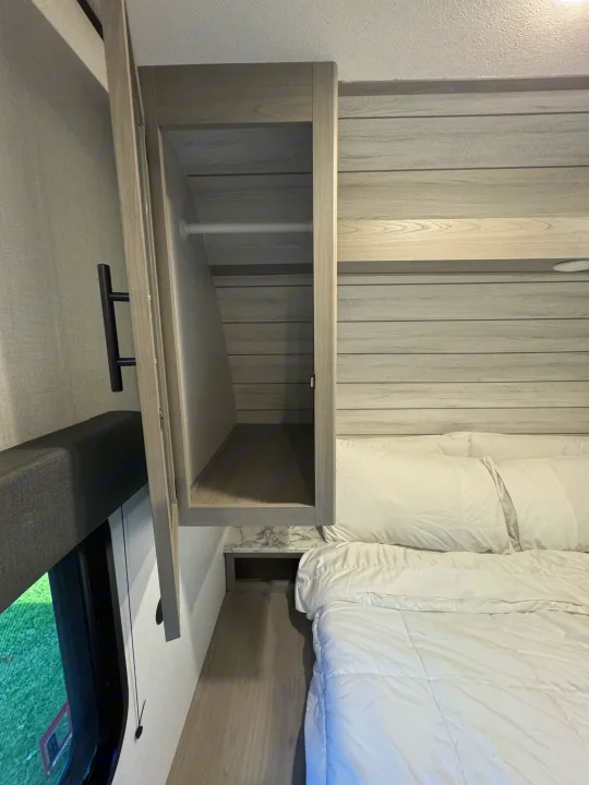 RV rental bedroom interior, showcasing a modern bed with white linens & an open wardrobe for compact storage.. Coleman Lantern 334BH 2024