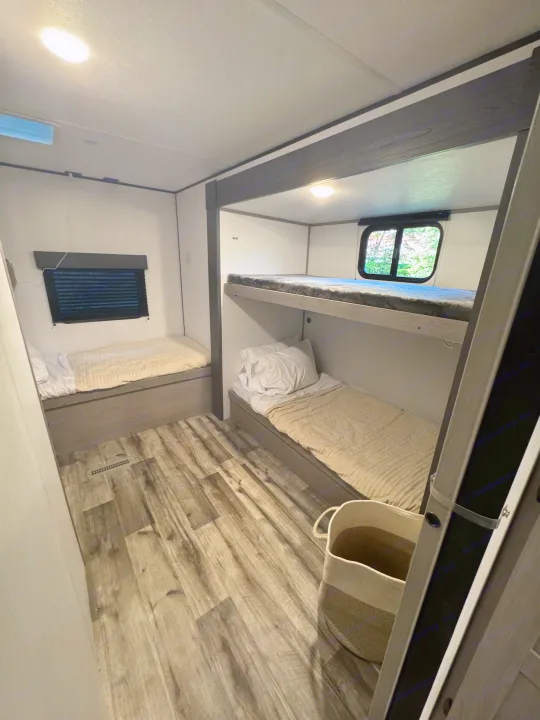 Interior of an RV rental showing a bright bunk room with two bunk beds, a single bed, wood-look flooring, and a window.. Coleman Lantern 334BH 2024
