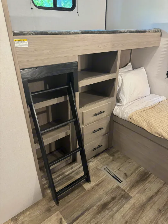 Modern RV rental interior featuring a bunk bed, ladder, lower bed, built-in shelves, and drawers for efficient storage and comfort.. Coleman Lantern 334BH 2024