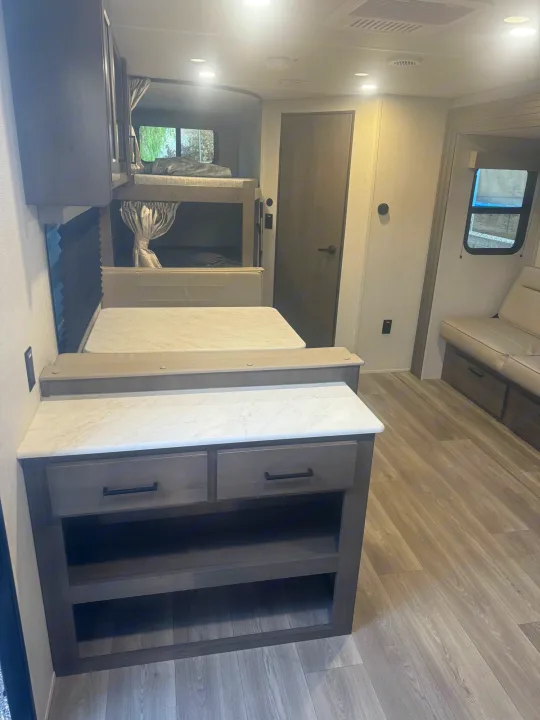 Modern RV rental interior with bunk beds, a dinette area, and functional counter space. Ready for adventures.. Grand Design Transcend Xplor 2024