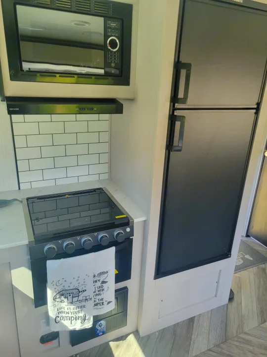 Inside an **rv rental**: a compact kitchen with microwave, range, fridge, and a tiled backsplash, ready for camping.. Heartland RVs Mallard 2023