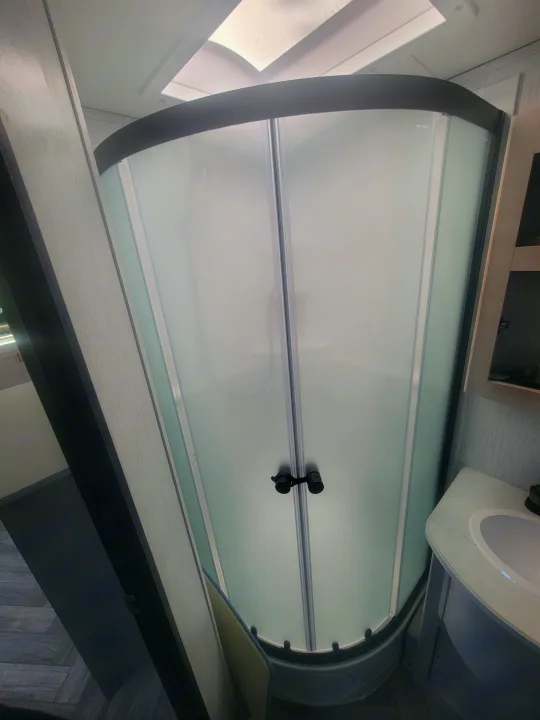 Step inside this RV rental's sleek bathroom. A compact corner shower with frosted glass doors and a bright skylight. Vanity sink visible.. Heartland RVs Mallard 2023