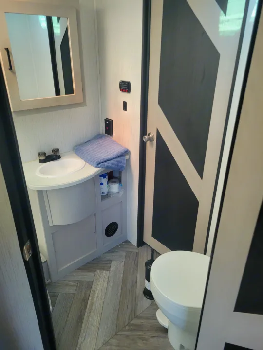 Inside an RV rental: a compact bathroom with vanity, sink, mirror, toilet, and modern wood-look flooring.. Heartland RVs Mallard 2023