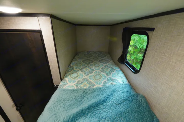This cozy RV rental sleeping area features a bed with patterned bedding, a window with views, and a nearby door.. Jayco Jay Flight 2022