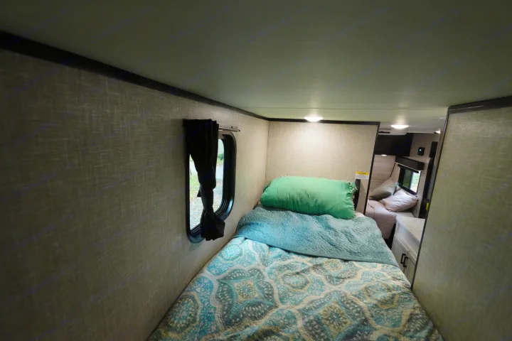 Step inside a cozy RV rental: a comfortable bunk bed area with soft bedding and natural light from a window.. Jayco Jay Flight 2022