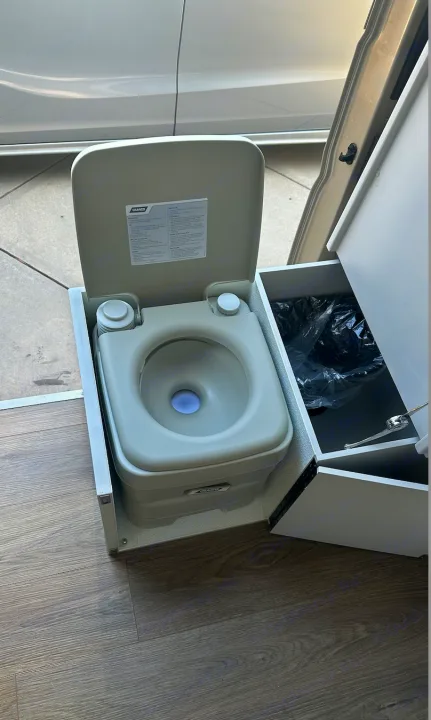 Inside the RV rental: a compact, portable toilet with adjacent storage for convenient mobile travel.. RAM Promaster 2024