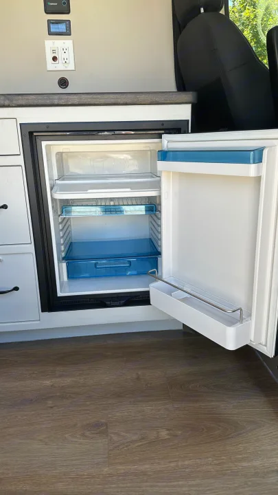 RV rental van interior with open mini-fridge, power outlets, and battery monitor showing 100%.. RAM Promaster 2024