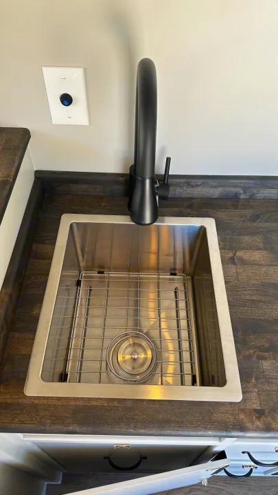 Sleek stainless steel sink and black faucet in an RV rental kitchen, complete with a dark counter and wall-mounted switch.. RAM Promaster 2024