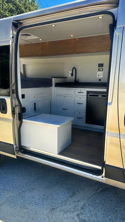 RV rental: Bright camper van interior with modern kitchen, bed, and storage. View from the open side door.. RAM Promaster 2024