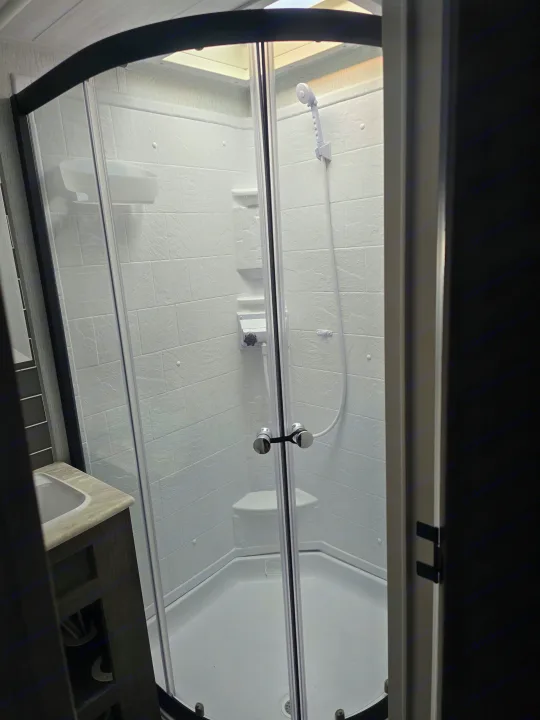 Clean, compact corner shower in an RV rental bathroom, with white tiled walls and a handheld showerhead.. Forest River Wildwood 2022