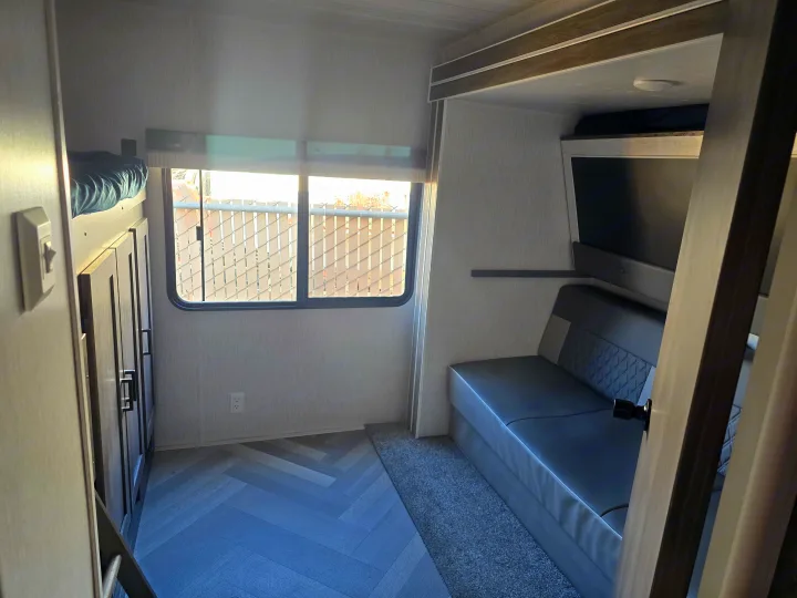 Cozy RV rental interior: bunk bed, window view of a fence, and gray sofa/dinette. Ideal for your next camper adventure.. Forest River Wildwood 2022