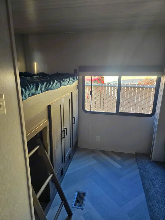 This RV rental features a cozy bunk bed setup with integrated storage, a window view, and stylish herringbone flooring.. Forest River Wildwood 2022