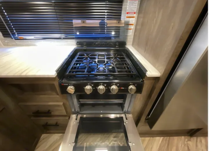 A modern RV rental kitchen featuring a black gas stove and oven with an open glass cover, ready for your road trip cooking.. Forest River Wildwood 2022