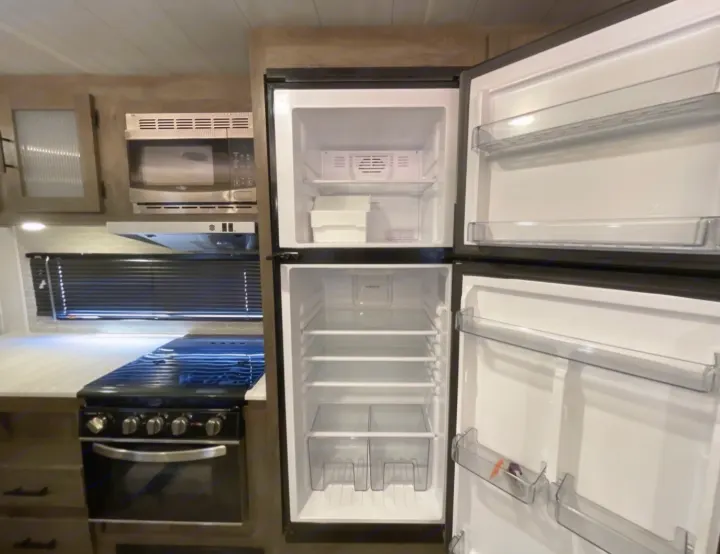 Clean RV rental kitchen featuring an open fridge, microwave, and stove.. Forest River Wildwood 2022