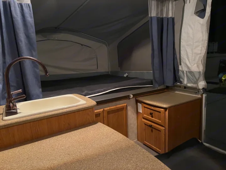 RV rental pop-up camper interior with a large bed, sink, and kitchen counter.. Forest River Palomino 2010