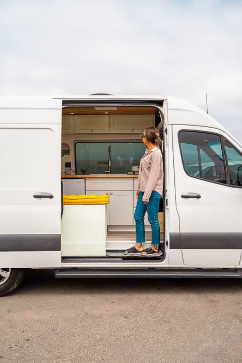 Step into adventure! A woman explores a modern RV rental's inviting, fully-equipped van kitchen.. Mercedes-Benz Sprinter 2019