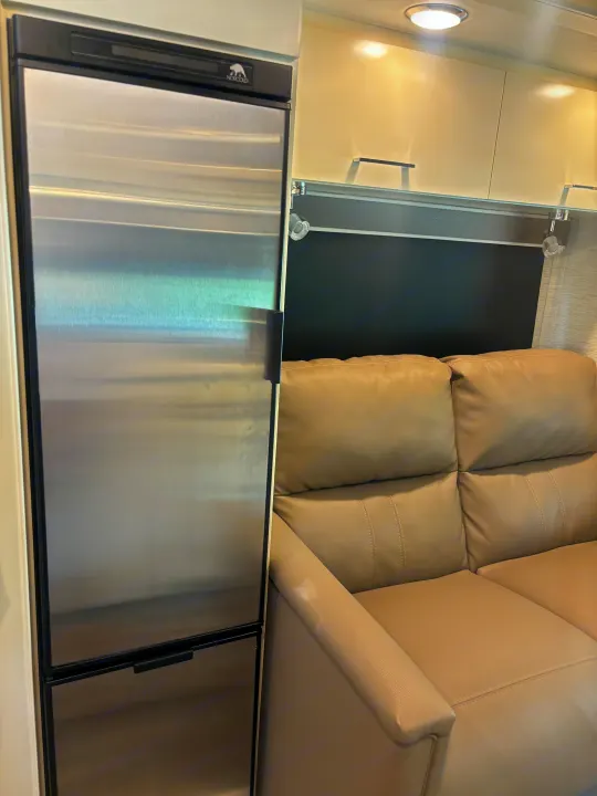 RV rental: Modern stainless steel refrigerator beside a light-colored reclining sofa in an RV interior.. Wayfarer Wayfarer Motorhome 2021