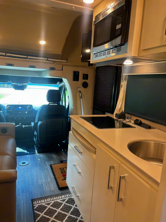 This modern camper van rv rental interior features a compact kitchenette with microwave, sink, and driver's cockpit.. Wayfarer Wayfarer Motorhome 2021