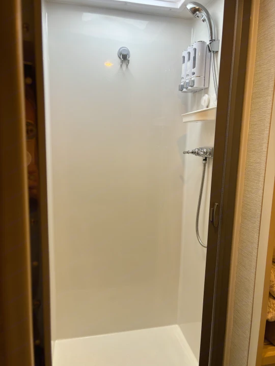 Clean, compact shower stall in an RV rental, featuring a shower head, soap dispenser, and small shelf.. Wayfarer Wayfarer Motorhome 2021