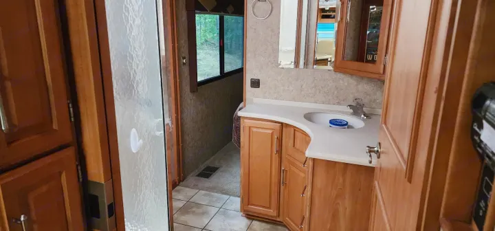RV rental interior showing a compact bathroom with shower, vanity, and sink, reflecting practical travel living.. Winnebago Journey 2006