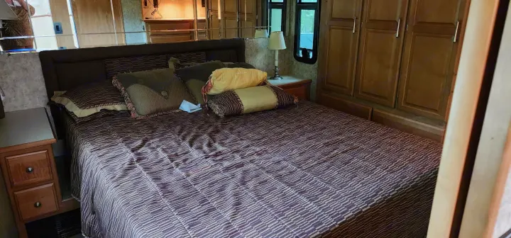 Cozy RV rental bedroom with a large bed, nightstand, and built-in cabinets. Mirrored headboard adds to the spacious feel.. Winnebago Journey 2006