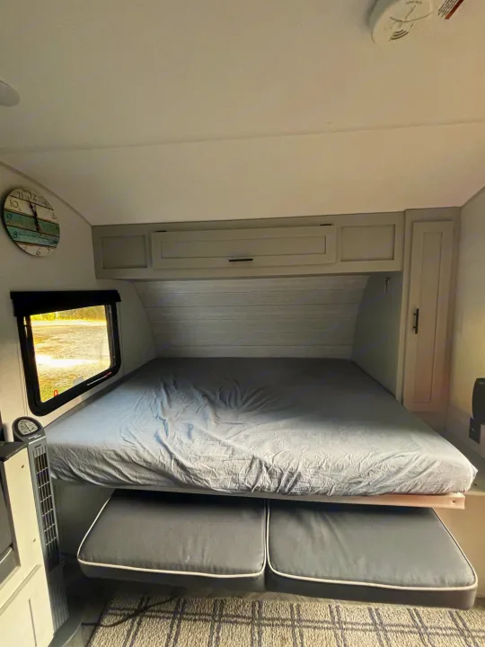 Experience comfort in this RV rental bedroom, featuring a large bed, under-bed seating, and functional overhead storage.. Forest River Wildwood FSX Plantium 2022