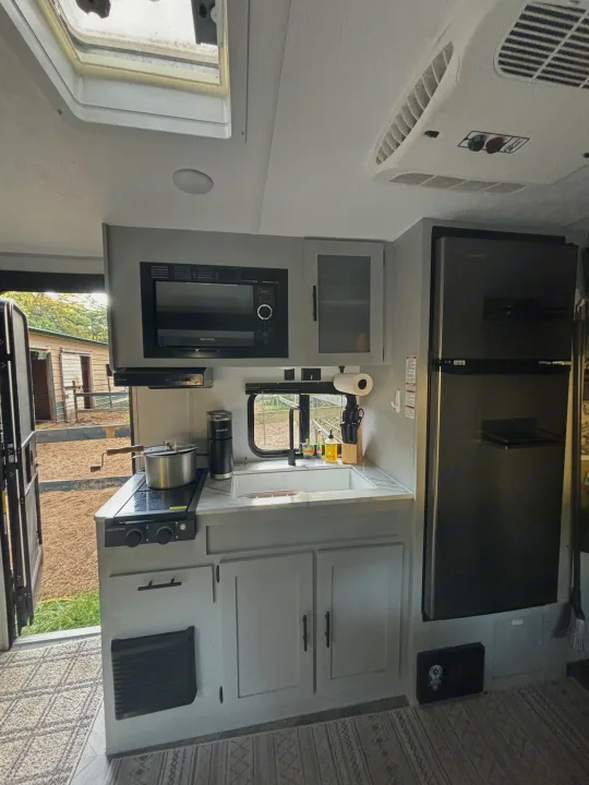 Modern RV rental kitchen features stove, sink, microwave, and fridge, ready for your travels.. Forest River Wildwood FSX Plantium 2022