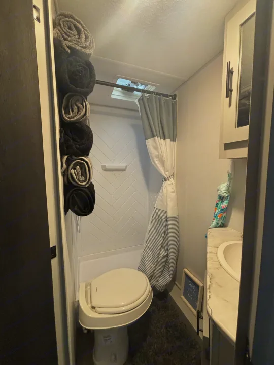 RV rental bathroom features a compact shower, toilet, sink, and stacked towels. Ideal for travel comfort.. Forest River Wildwood FSX Plantium 2022