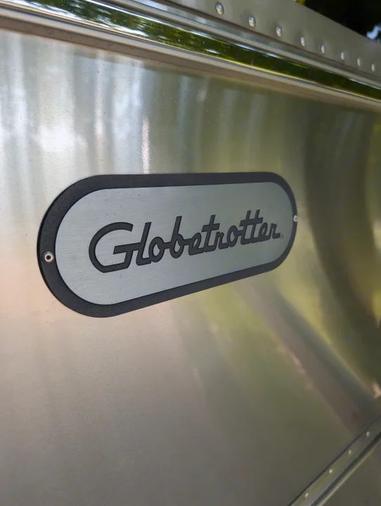 Close-up of a silver "Globetrotter" Airstream RV, ideal for rv rental. Reflections of green foliage on the polished aluminum.. Airstream Globetrotter 2024