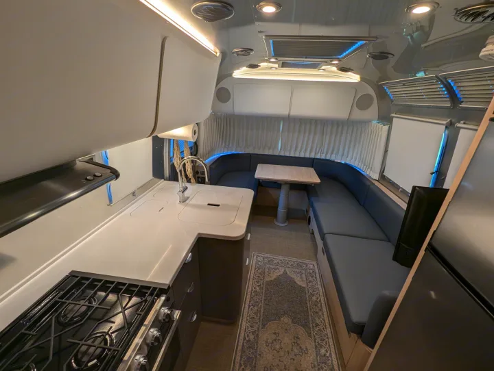 Modern RV rental interior with a full kitchen on the left and a U-shaped dining area on the right.. Airstream Globetrotter 2024