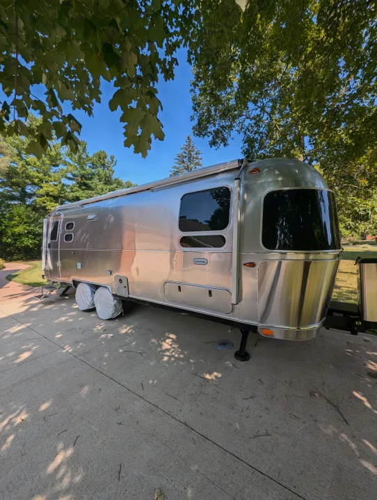 This beautiful silver Airstream RV rental is ready for your next escape, parked on concrete under trees.. Airstream Globetrotter 2024